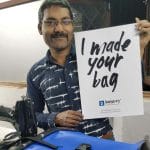 A worker at Jaggery holds up a sign that says "I made your bag." He is just one of the employees who create fair trade, high quality branded logo bags.