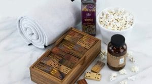 Corporate gifts that give back: A gift set comprised of handmade dominoes in an engravable box, popcorn, and a rolled blanked made from recycled bottles