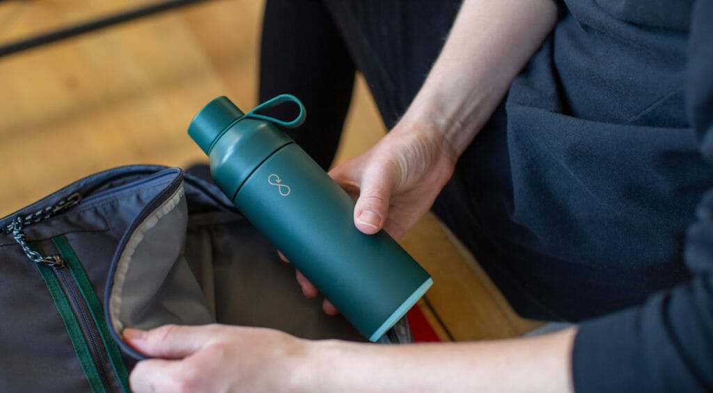 Best custom water bottles with logo, shown with a hand taking it from a backpack pouch