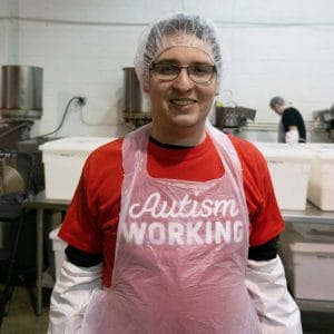 Our domino game gift set includes popcorn created by workers on the autism spectrum, like this man in an apron wearing a red shirt that says Autism WORKING.