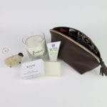 The pampering gift basket contains a leather pouch, body butter, soap, a glass candle, and a sheep ornament.