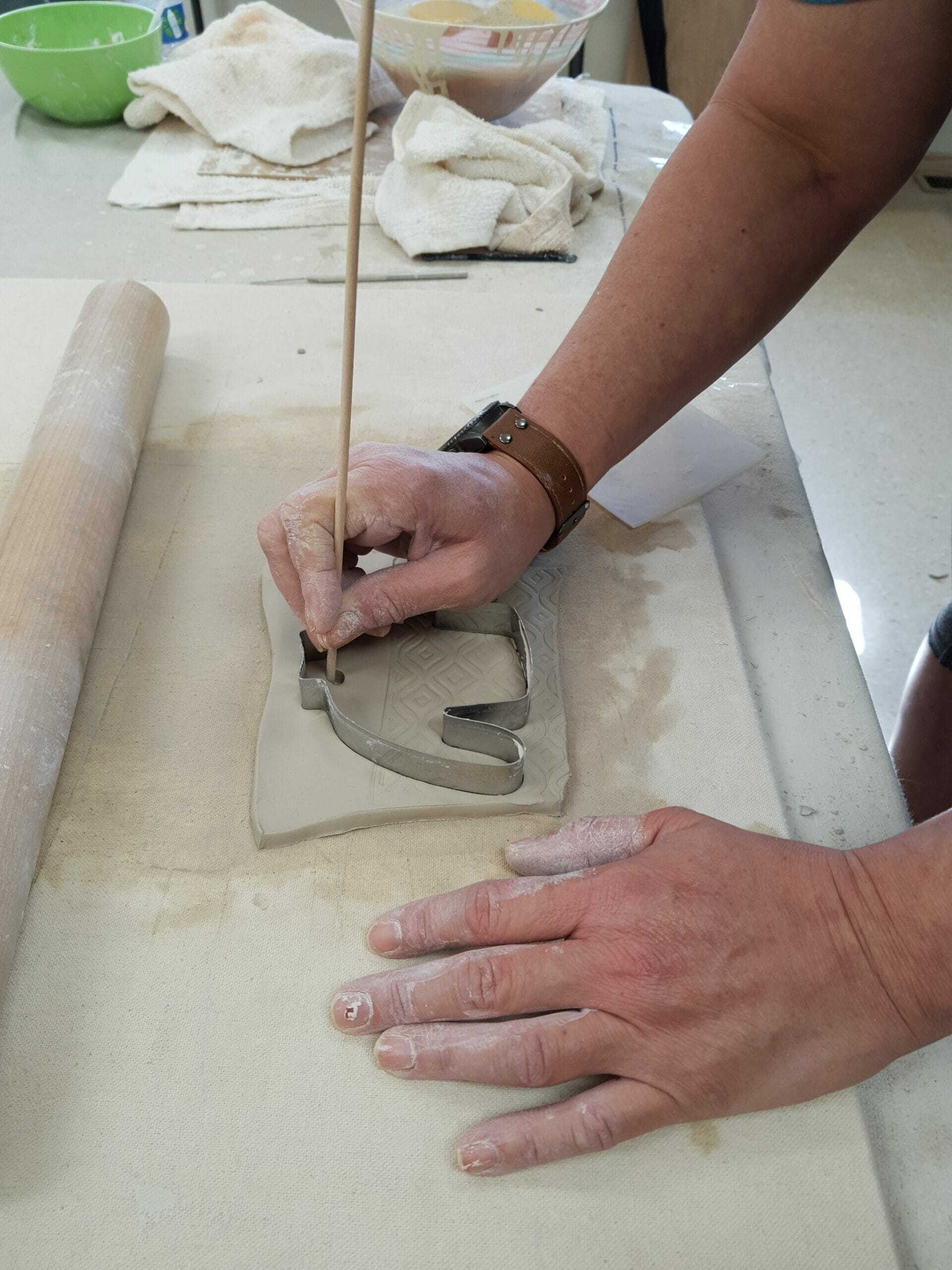 A maker pokes a hole for the string in the clay of an ugly sweater ornament