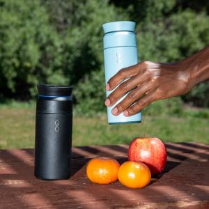 Two personalized stainless steel travel mugs, one black on the table, and one blue being gripped by a hand.