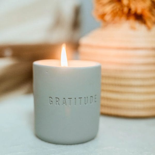 Lit gratitude candle in front of a vase
