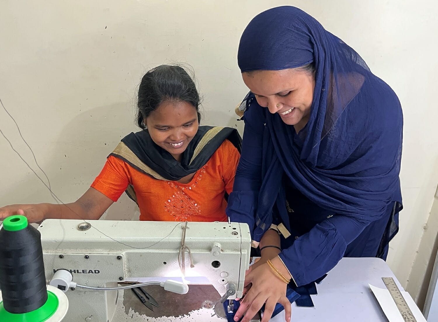 Two smiling women working together on a sewing machine